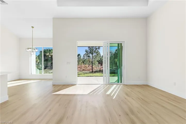 Spare room featuring a chandelier, light wood finished floors, healthy amount of natural light, and a high ceiling