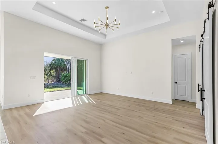 Unfurnished room with a barn door, hanging lights, a tray ceiling, and light wood-type flooring