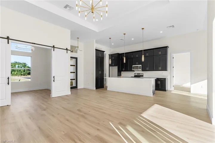 Kitchen featuring open floor plan, dark cabinets, light countertops, an island with sink, and a raised ceiling