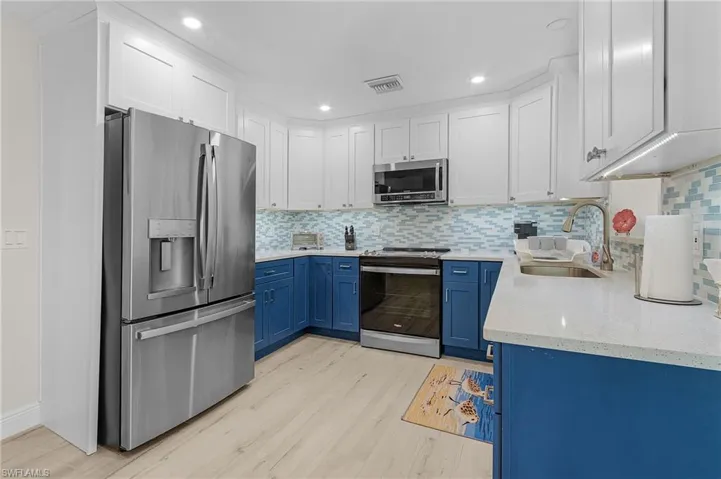 Kitchen with light wood-type flooring, stainless steel appliances, blue cabinets, sink, and white cabinetry
