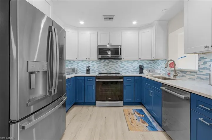 Kitchen with white cabinets, sink, light wood-type flooring, blue cabinetry, and stainless steel appliances