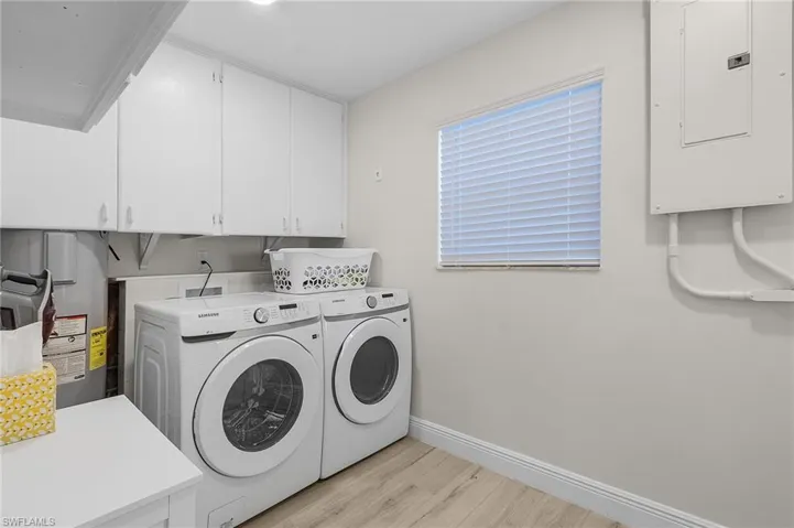 Washroom featuring cabinets, electric panel, electric water heater, washer and clothes dryer, and light hardwood / wood-style floors