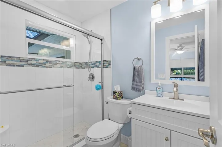 Bathroom featuring ceiling fan, toilet, an enclosed shower, and vanity