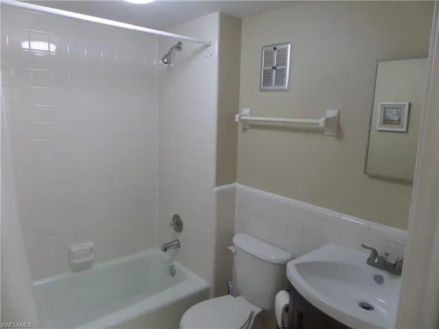 Full bathroom with tiled shower / bath, vanity, toilet, and tile walls