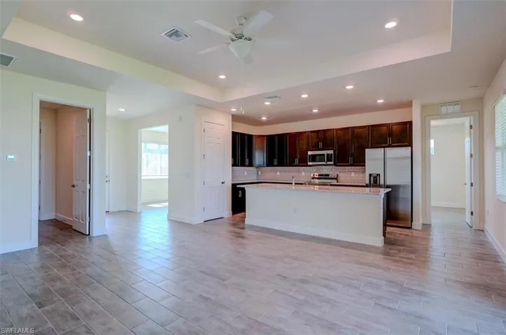 Kitchen with ceiling fan, tasteful backsplash, a raised ceiling, appliances with stainless steel finishes, and a kitchen island with sink