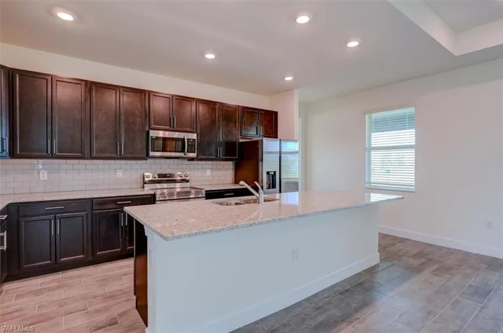 Kitchen featuring stainless steel appliances, a center island with sink, sink, backsplash, and light stone countertops