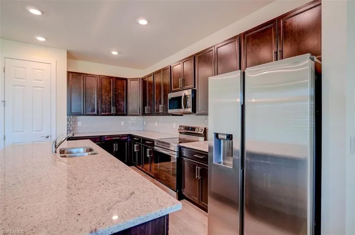 Kitchen with light wood-type flooring, stainless steel appliances, light stone countertops, decorative backsplash, and sink