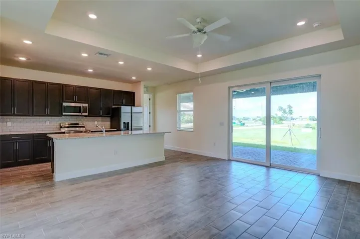 Kitchen featuring backsplash, ceiling fan, a tray ceiling, appliances with stainless steel finishes, and a center island with sink
