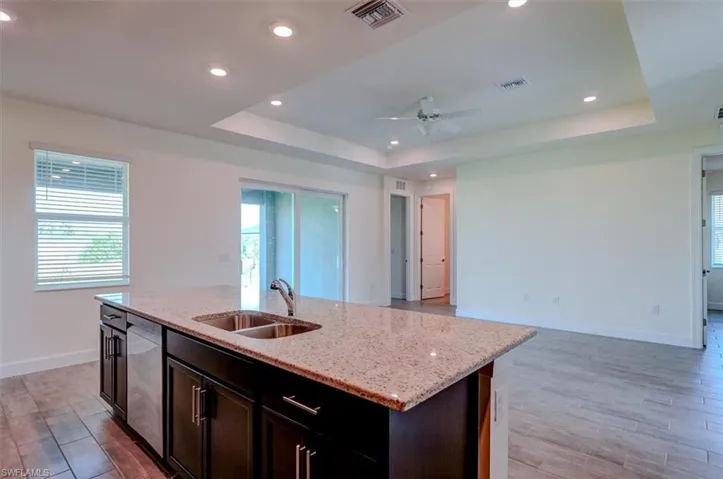 Kitchen with sink, ceiling fan, a raised ceiling, and an island with sink