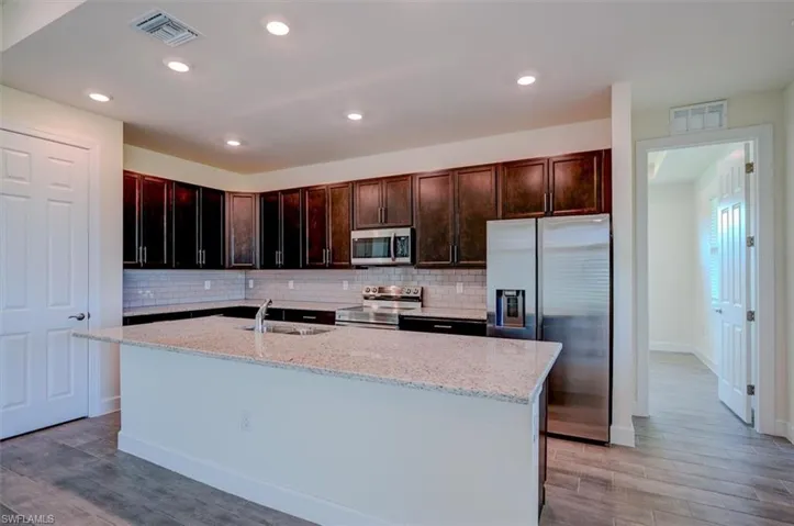 Kitchen with hardwood / wood-style flooring, sink, light stone counters, and stainless steel appliances