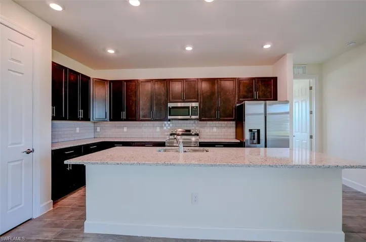 Kitchen featuring backsplash, light stone countertops, appliances with stainless steel finishes, sink, and a center island with sink