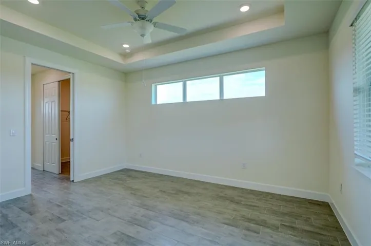 Spare room with a tray ceiling, light hardwood / wood-style flooring, and ceiling fan