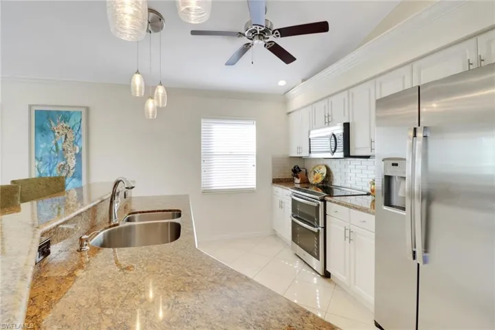 Kitchen with sink, light tile patterned floors, stainless steel appliances, white cabinets, and decorative light fixtures