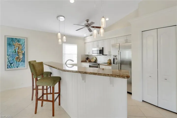 Kitchen featuring appliances with stainless steel finishes, white cabinetry, backsplash, hanging light fixtures, and a kitchen bar