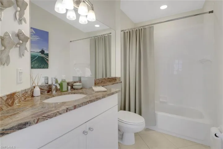 Full bathroom with shower / bathtub combination with curtain, vanity, tile patterned floors, toilet, and a chandelier