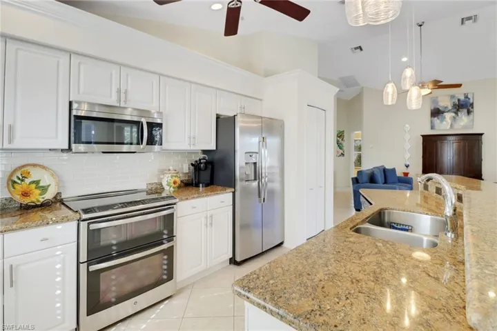 Kitchen with pendant lighting, sink, white cabinets, light stone counters, and stainless steel appliances