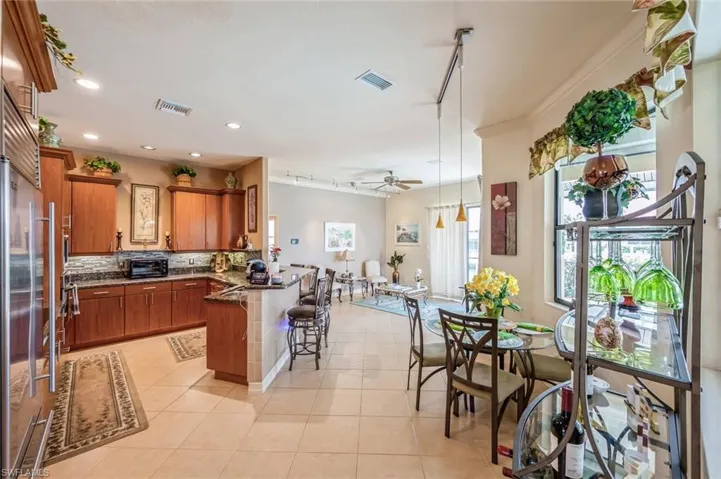 Kitchen featuring kitchen peninsula, ceiling fan, rail lighting, a kitchen bar, and light tile floors