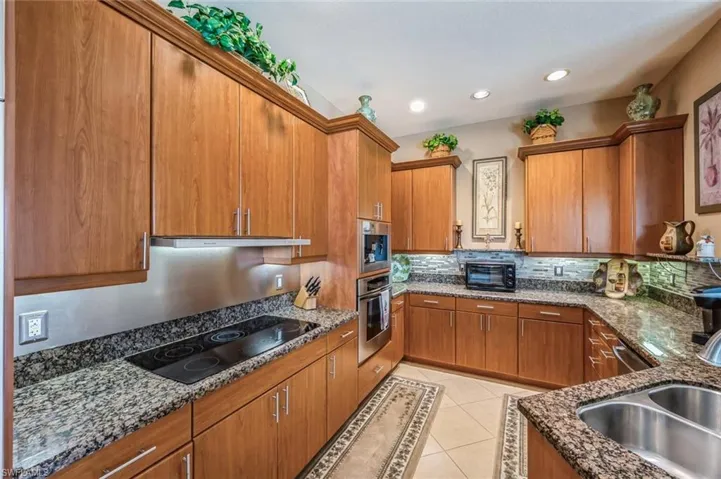 Kitchen with dark stone counters, oven, black electric cooktop, sink, and light tile floors