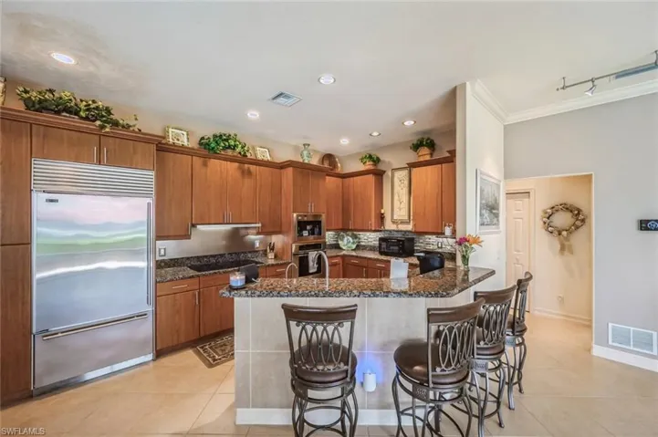 Kitchen featuring ornamental molding, black appliances, dark stone counters, kitchen peninsula, and light tile floors