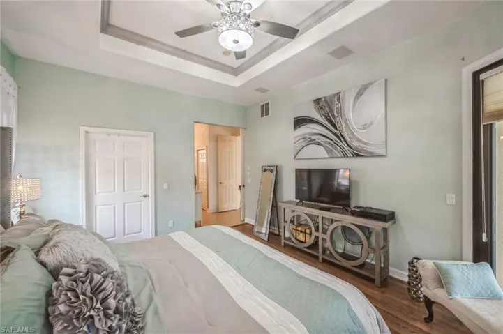 Bedroom with ceiling fan, a tray ceiling, and hardwood / wood-style flooring