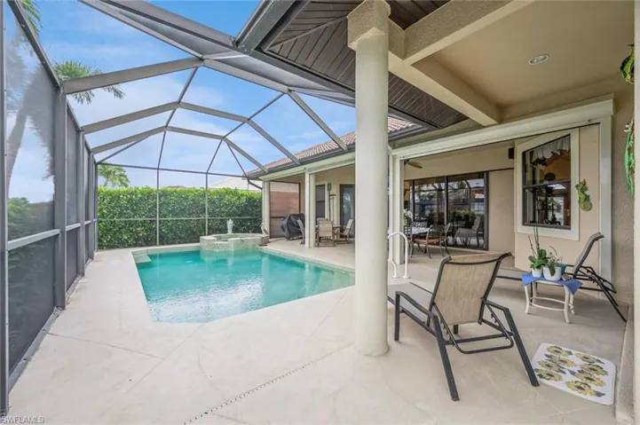 View of swimming pool featuring a patio, glass enclosure, and an in ground hot tub