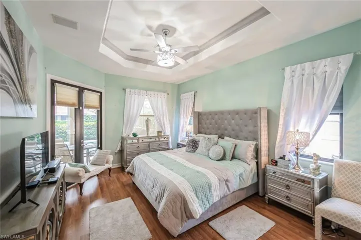 Bedroom with dark wood-type flooring, ceiling fan, and a raised ceiling