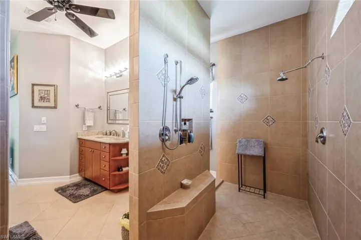 Bathroom with tile floors, ceiling fan, tiled shower, and vanity