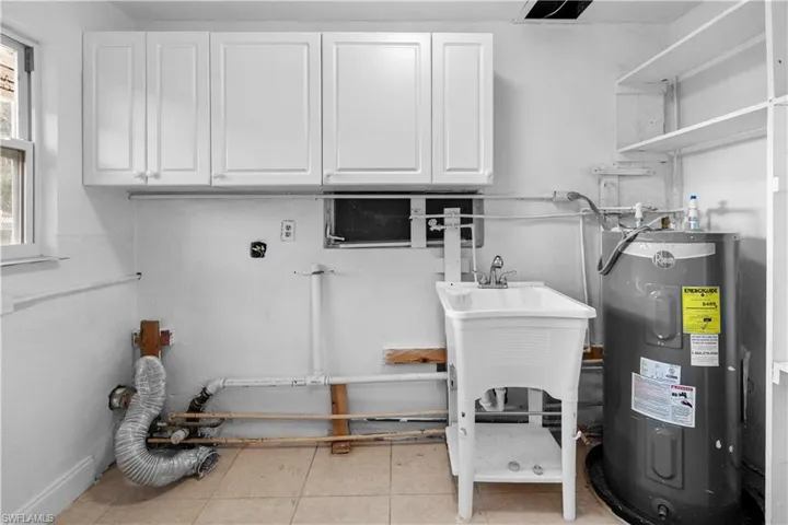 Laundry area featuring electric water heater and cabinet space