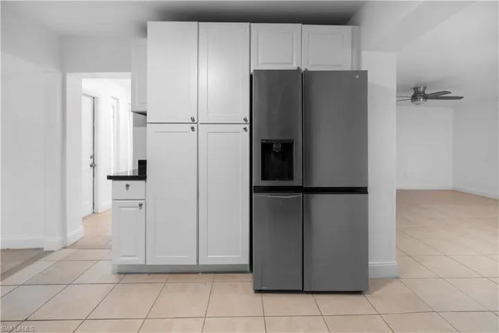 Kitchen with stainless steel fridge, white cabinets, ceiling fan, light tile patterned flooring, and dark countertops