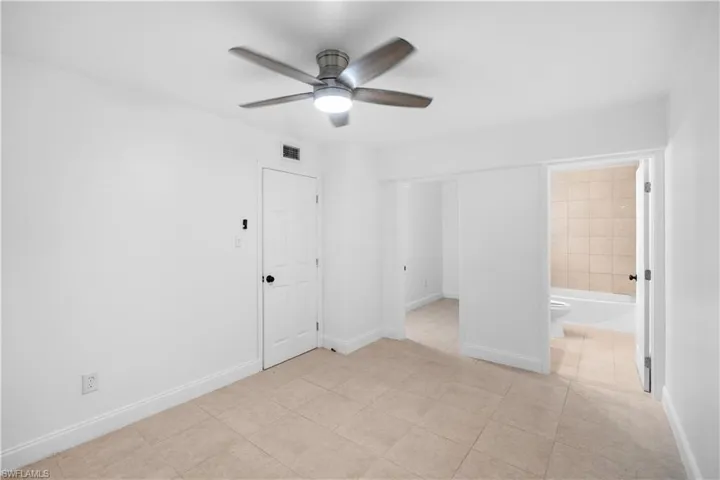 Unfurnished bedroom featuring ceiling fan, light tile patterned floors, and ensuite bath