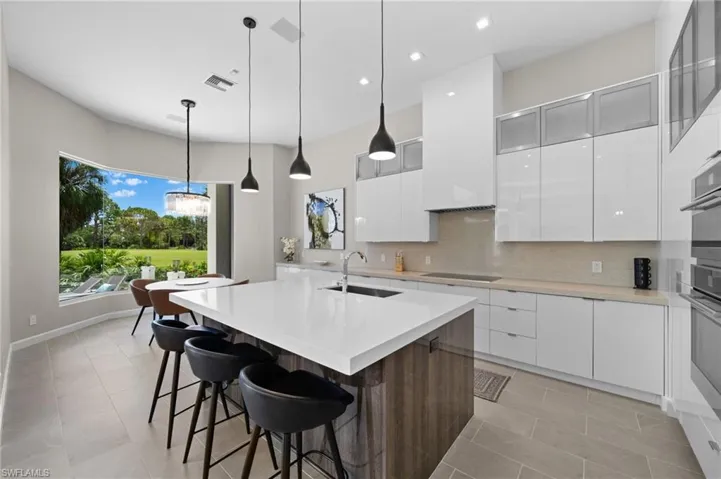 Kitchen with white cabinetry, hanging light fixtures, a center island with sink, black electric cooktop, and sink