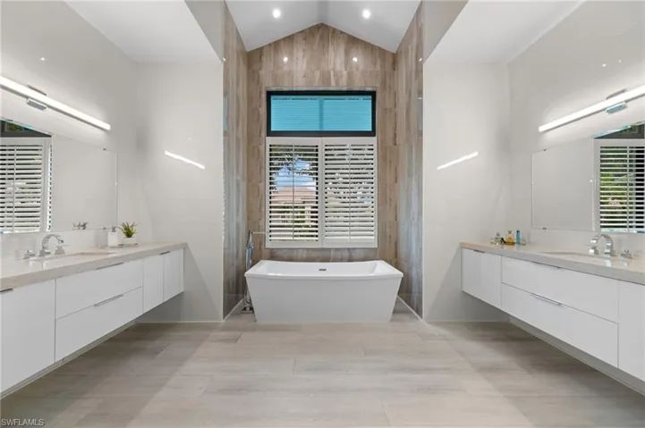 Bathroom with a bathtub, tile flooring, vanity, and vaulted ceiling