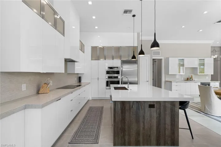Kitchen with hanging light fixtures, stainless steel appliances, an island with sink, white cabinets, and tasteful backsplash