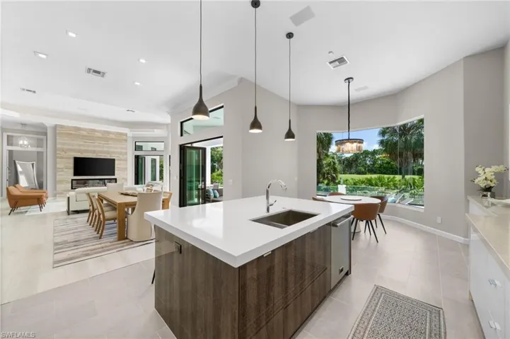 Kitchen with a center island with sink, dark brown cabinets, decorative light fixtures, sink, and light tile flooring