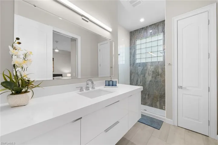 Bathroom with tile flooring, ceiling fan, tiled shower, and vanity