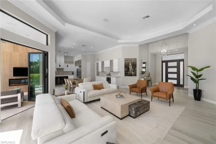 Living room with a tray ceiling, a wealth of natural light, light wood-type flooring, and an inviting chandelier