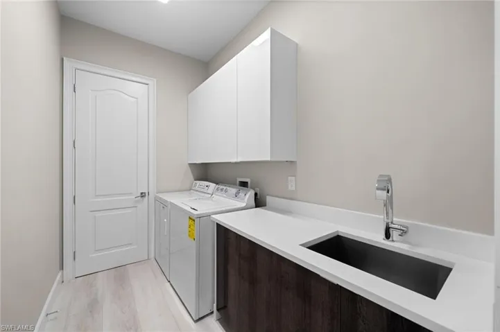 Clothes washing area featuring washer and dryer, cabinets, light hardwood / wood-style floors, washer hookup, and sink