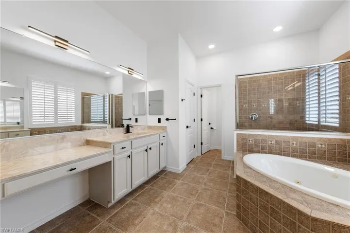 Dual vanity with light-toned countertops and integrated sink, full-width mirror, white cabinetry, and contemporary lighting fixtures