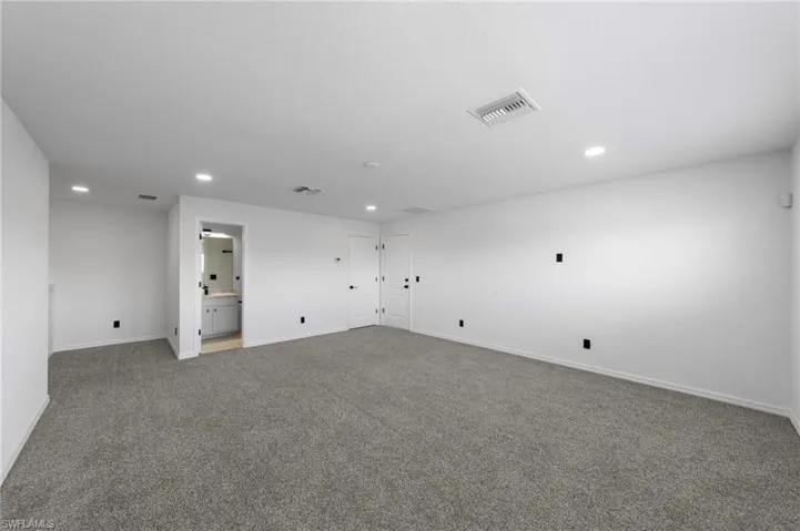 Expansive carpeted area with recessed lighting, an interior doorway with black hardware, and an alcove featuring a vanity with a rectangular sink