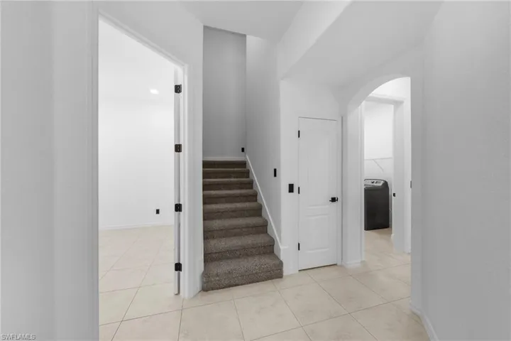 Tiled flooring throughout the main level, staircase with carpeted treads, white interior doors with dark hardware, and an arched entryway
