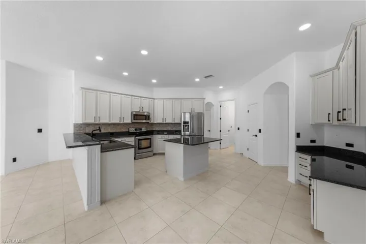 Kitchen featuring light-toned cabinetry, stainless steel appliances, dark countertops, a central island, and tiled flooring