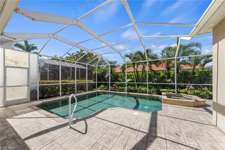 Screened pool enclosure featuring a swimming pool, integrated spa, and stamped concrete patio