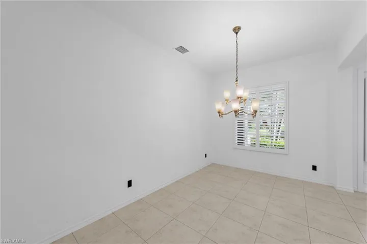Recessed ceiling with a multi-arm chandelier, large window with plantation shutters, and square tile flooring