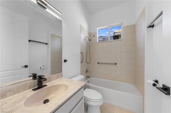 Vanity with integrated sink and dark bronze faucet, framed mirror, and built-in bathtub with tiled surround
