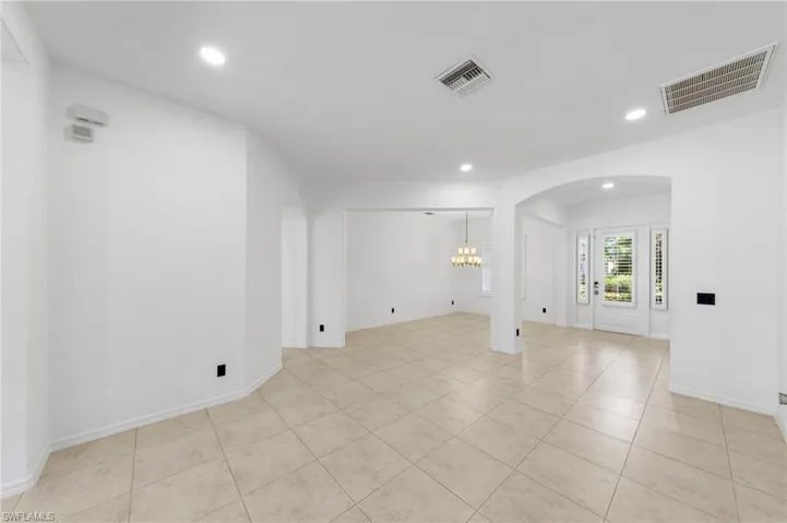 Recessed lighting, arched doorways, tiled flooring, front entry door with sidelights, and a chandelier in the background
