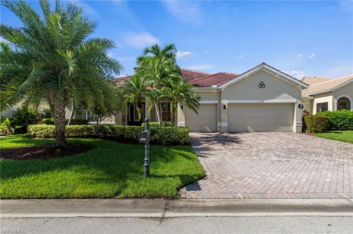 Stucco exterior with a tile roof, paver driveway, and an attached two-car garage