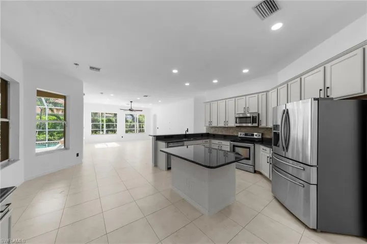Open-concept kitchen featuring an island with dark countertops, light cabinetry, stainless steel appliances, and tile flooring