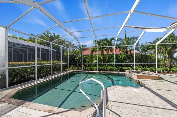 Screened outdoor swimming pool with an integrated spa, surrounded by a textured concrete pool deck and lush landscaping