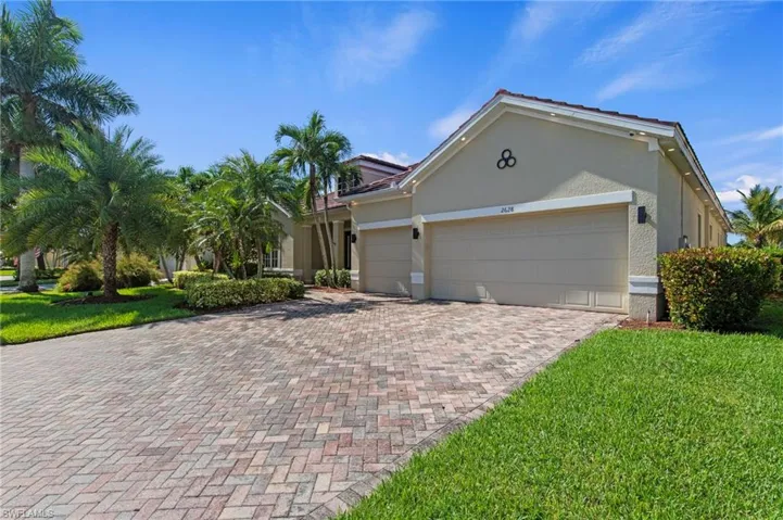 Paver driveway, lush landscaping, two-car garage, red tile roof, and stucco exterior