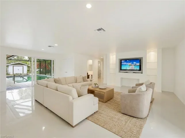 Open-concept living area featuring a built-in entertainment center with integrated shelving, recessed lighting, and large sliding glass doors opening to an outdoor swimming pool
